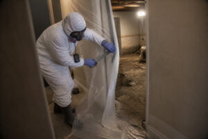 technician in full protective gear setting up containment barrier during biohazard cleanup in basement