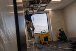 technicians repairing water damage and measuring moisture in commercial office ceiling during restoration in South Jordan Utah