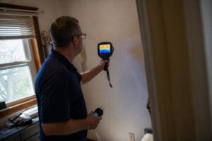 technician using thermal imaging camera to detect hidden moisture behind wall during inspection in Utah home